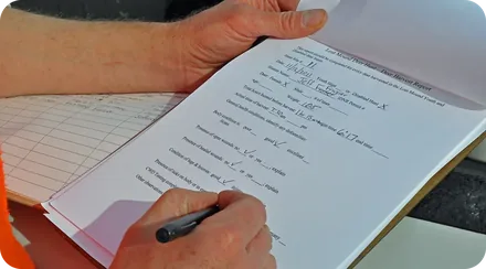 Primer plano de una mano repasando con bolígrafo una lista impresa de comparación de planes sobre un escritorio