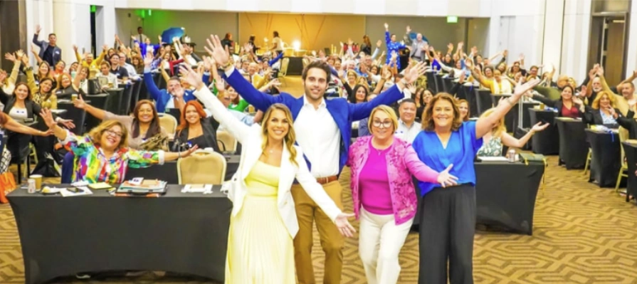 A packed ballroom of agents with their arms raised at a past Madrinas AEP kickoff