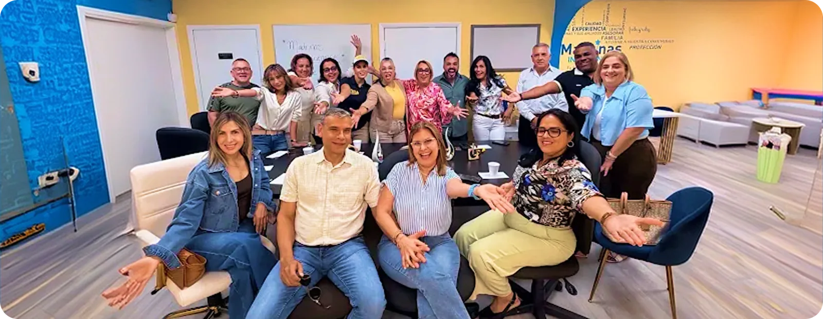 Unas quince personas del equipo de Madrinas posan juntas con los brazos abiertos en su luminosa oficina de Miami, algunas sentadas en sillas blancas al frente y otras de pie detrás, entre una pared amarilla y una pared azul