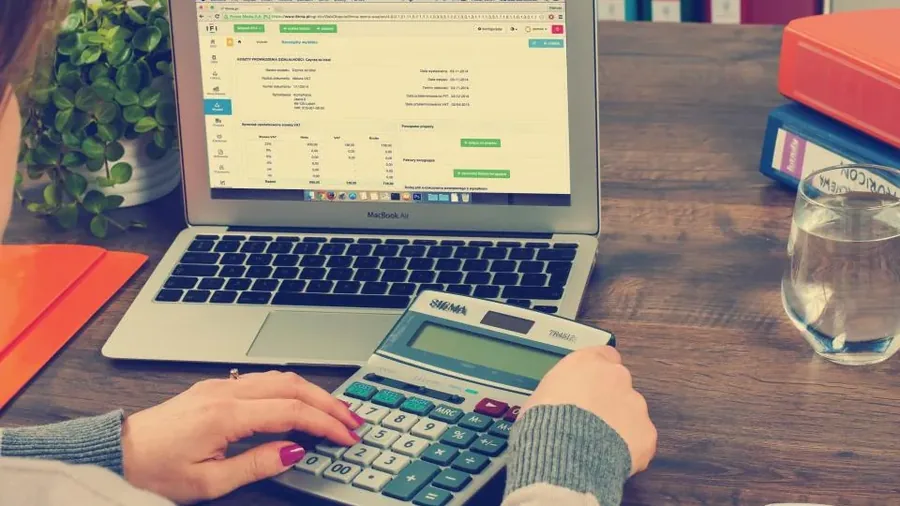 Hands working a desktop calculator beside an open laptop and notebook
